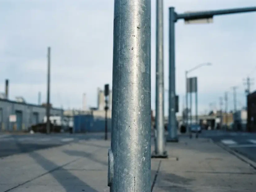 Gegalvaniseerde stalen lichtmast op betonnen stoep, gefotografeerd vanuit lage hoek met bokeh op achtergrond.